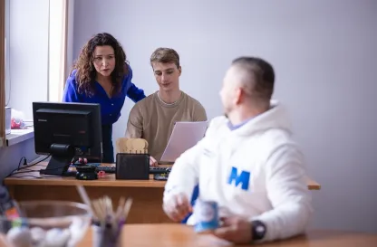 Aktualności | Uniwersytet WSB Merito Bydgoszcz: student odwrócony w kierunku dwójki studentów siedzących przy komputerze