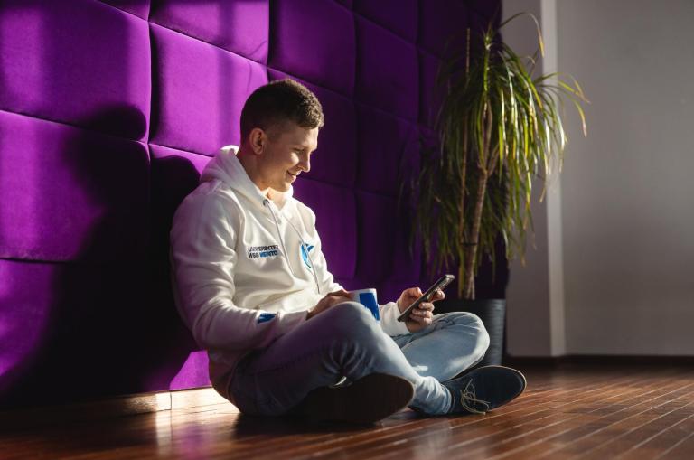Studia I stopnia w Bydgoszczy | Uniwersytet WSB Merito Bydgoszcz: student Uniwersytetu WSB Merito Bydgoszcz siedzi na podłodze z telefonem w ręku