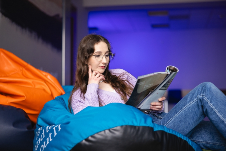Student Council | WSB Merito Bydgoszcz University: Dziewczyna siedzi na sofie w strefie studenta na uczelni i czyta książkę