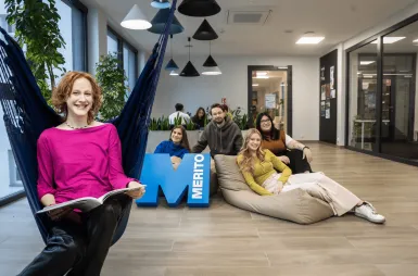 The student ABC | WSB Merito Gdańsk University: Studentka na hamaku siedzi z książką, za nią grupa studentów z sygnetem M