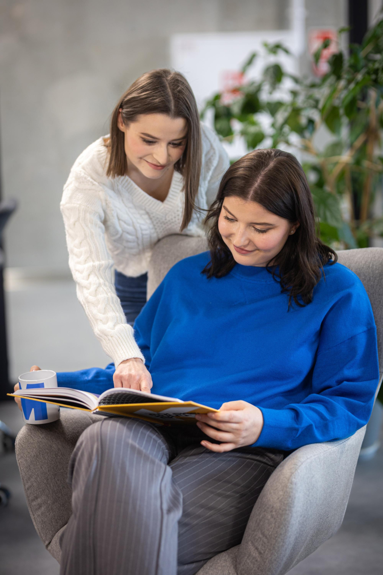Search results | WSB Merito Gdańsk University: Studentka siedząca na fotelu z książką i pochylająca się nad nią dziewczyna i pokazująca coś w publikacji