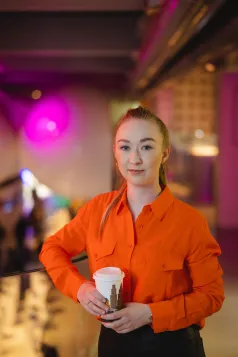 Student Council | WSB Merito Poznań University: Studentka w pomarańczowej koszuli pozuje z kubkiem kawy