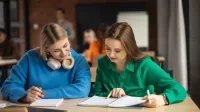 Psychologia w marketingu | Studia I stopnia w Gdańsku | Uniwersytet WSB Merito w Gdańsku: dwie dziewczyny siedzą przy biurku i pochylają się nad zeszytami