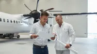 Obsługa ruchu lotniczego | Studia I stopnia w Gdańsku | Uniwersytet WSB Merito w Gdańsku: Dwóch ubranych na jasno mężczyzn patrzy na kartkę i znajdują się w przestrzeni, gdzie jest samolot