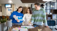 Dwie studentki i student stoją nad stołem i wykonują zadanie