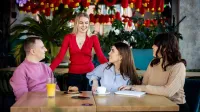 Menedżer hotelu i restauracji | Studia I stopnia w Gdańsku | Uniwersytet WSB Merito w Gdańsku: Studenci znajdujący się w kawiarni. Trzech z nich siedzi przy stoliku, a jedna osoba nad nimi stoi - rozmawiają