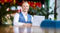Administracja i biznes | Studia II stopnia w Gdańsku | Uniwersytet WSB Merito w Gdańsku: Student przy stoliku z laptopem. Jest ubrany biznesowo w koszulę i marynarkę w kratkę