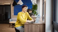 Projektowanie graficzne | Studia I stopnia w Gdańsku | Uniwersytet WSB Merito w Gdańsku: Student siedzi przy laptopie, ma na sobie żółty sweter i fioletową czapkę
