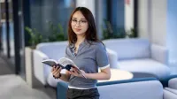 Dziennikarstwo międzynarodowe | Studia I stopnia w Gdańsku | Uniwersytet WSB Merito w Gdańsku: Studentka o azjatyckiej urodzie opiera się o kanapę i trzyma książkę