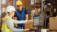 Logistyka i spedycja | Studia I stopnia w Gdańsku | Uniwersytet WSB Merito w Gdańsku: Kobieta i mężczyzna w kaskach na magazynie sprawdzają coś na komputerze