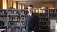 Administracja i biznes | Studia II stopnia ze studiami podyplomowymi w Gdańsku | Uniwersytet WSB Merito w Gdańsku: Student w bibliotece ubrany w garnitur 