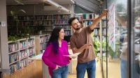 Terapia pedagogiczna z elementami integracji sensorycznej | Studia II stopnia w Gdańsku | Uniwersytet WSB Merito w Gdańsku: Student z wykładowczynią przy tablicy znajdującej się w bibliotece