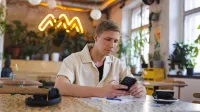 Programowanie | Studia I stopnia w Gdańsku | Uniwersytet WSB Merito w Gdańsku: Student przy telefonie w kawiarni 