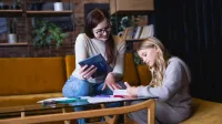 Przygotowanie pedagogiczne dla psychologów | Studia podyplomowe w Gdańsku | Uniwersytet WSB Merito w Gdańsku: Kobieta pomaga dziewczynce przy odrabianiu pracy domowej