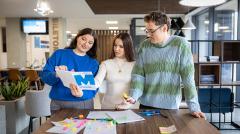 Dwie studentki i student stoją nad stołem i wykonują zadanie