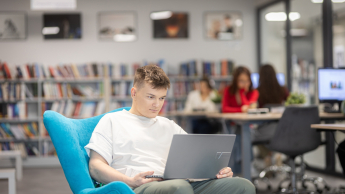 Prompting i optymalizacja systemów AI | Studia I stopnia w Gdańsku | Uniwersytet WSB Merito w Gdańsku: Student siedzi na fotelu z laptopem na kolanach w bibliotece