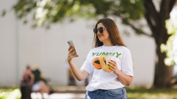 Komunikacja cyfrowa i media kreatywne | Studia II stopnia ze studiami podyplomowymi w Gdańsku | Uniwersytet WSB Merito w Gdańsku: Studentka latem z komórką i napojem w ręku