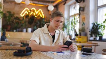 Programowanie | Studia I stopnia w Gdańsku | Uniwersytet WSB Merito w Gdańsku: Student przy telefonie w kawiarni 