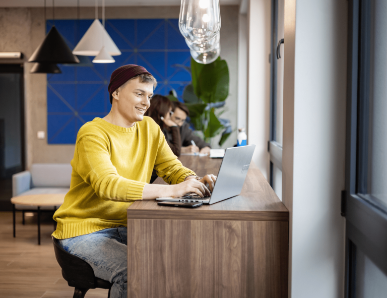 Programowanie desktop apps | Studia II stopnia w Gdańsku | Uniwersytet WSB Merito w Gdańsku: Student siedzi przy laptopie, ma na sobie żółty sweter i fioletową czapkę