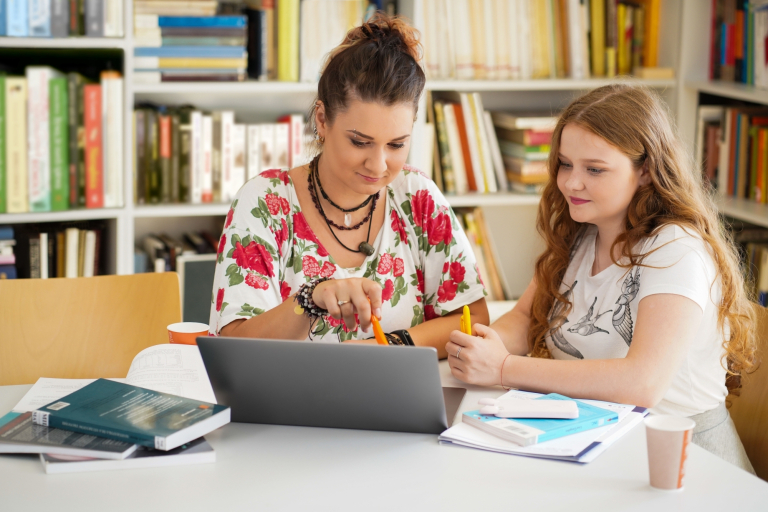Pedagogika opiekuńczo-wychowawcza z proﬁlaktyką społeczną | Studia II stopnia w Gdańsku | Uniwersytet WSB Merito w Gdańsku: Zdjęcie kobiety pokazującej coś w laptopie młodej dziewczynce
