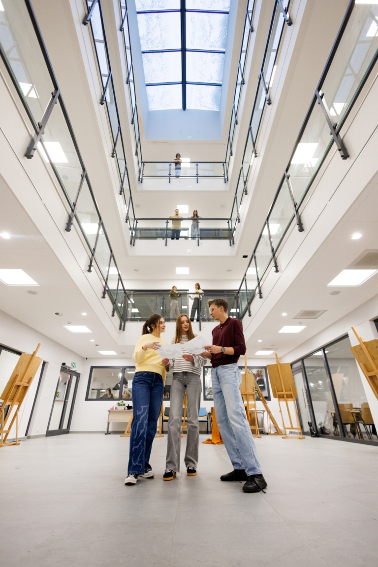 Marketing i komunikacja społeczna | Studia II stopnia w Gdańsku | Uniwersytet WSB Merito w Gdańsku: Studenci stoją pośrodku atrium. Zdjęcie z perspektywy żabiej z widokiem na architekturę budynku