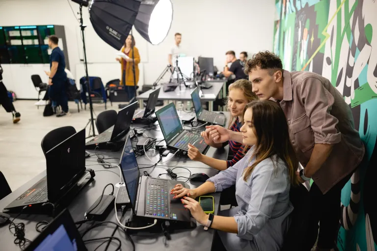 Bezpieczeństwo systemów informatycznych | Studia I stopnia w Gdańsku | Uniwersytet WSB Merito w Gdańsku: Studenci w studio z komputerami, lampami i grafiką na ścianie