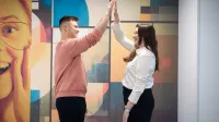 Tłumaczenia – język angielski | Studia I stopnia w Gdyni | Uniwersytet WSB Merito Gdynia: studenci przybijający sobie piątkę na tle kolorowej fototapety