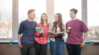 Tłumaczenia – język angielski | Studia I stopnia w Gdyni | Uniwersytet WSB Merito Gdynia: Zdjęcie studentów opierających się o parapet, z tyłu świeci słońce. Na zdjęciu znajduje się dwóch chłopaków i dwie dziewczyny, które zajmują centralne miejsce i trzymają książki