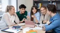 Terapia pedagogiczna z elementami arteterapii | Studia I stopnia w Gdyni | Uniwersytet WSB Merito Gdynia: studenci siedzą przy stole rozmawiając i pracując nad projektem