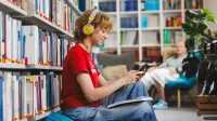 Psychologia reklamy i komunikacji | Studia podyplomowe w Gdyni | Uniwersytet WSB Merito Gdynia: Studentka ze słuchawkami w uszach, książką na kolanach i telefonem w ręku