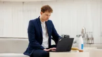 Agent celny | Studia podyplomowe w Gdyni | Uniwersytet WSB Merito Gdynia: Mężczyzna w garniturze przy laptopie w jasnej przestrzeni