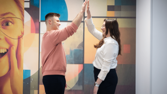 Tłumaczenia – język angielski | Studia I stopnia w Gdyni | Uniwersytet WSB Merito Gdynia: studenci przybijający sobie piątkę na tle kolorowej fototapety