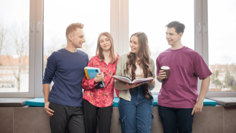 Tłumaczenia – język angielski | Studia I stopnia w Gdyni | Uniwersytet WSB Merito Gdynia: Zdjęcie studentów opierających się o parapet, z tyłu świeci słońce. Na zdjęciu znajduje się dwóch chłopaków i dwie dziewczyny, które zajmują centralne miejsce i trzymają książki