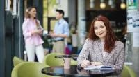 Digital marketing | Studia II stopnia w Łodzi | Uniwersytet WSB Merito Łódź: Studentka zapisuje notatki, a obok stoi kawa.