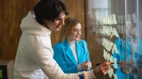 Zarządzanie | Studia I stopnia w Łodzi | Uniwersytet WSB Merito Łódź: Dwoje studentów pracuje wspólnie przy szklanej tablicy z karteczkami, planując i omawiając elementy projektu.