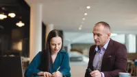 Kobieta i mężczyzna siedzą przy stole w nowoczesnym wnętrzu, wspólnie analizując notatki i dokumenty.