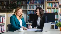 Organizacja i zarządzanie oświatą | Studia podyplomowe w Łodzi | Uniwersytet WSB Merito Łódź: uczestniczki przy stole w bibliotece pracują i przeglądają dokumenty 