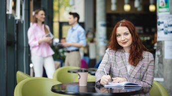 Digital marketing | Studia II stopnia w Łodzi | Uniwersytet WSB Merito Łódź: Studentka zapisuje notatki, a obok stoi kawa.