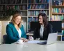 Weź udział w sesji zdjęciowej na Uniwersytecie WSB Merito | Aktualności | Uniwersytet WSB Merito Łódź: uczestniczki przy stole w bibliotece pracują i przeglądają dokumenty 