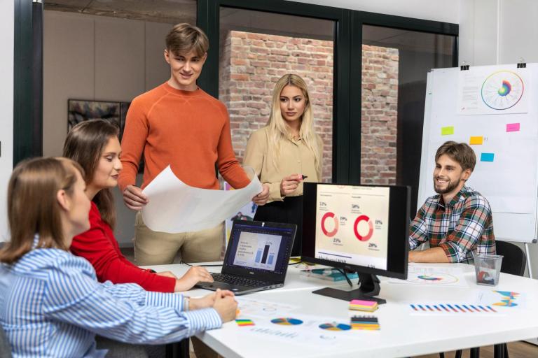 Transport, spedycja i magazynowanie | Studia I stopnia w Łodzi | Uniwersytet WSB Merito Łódź: Grupa młodych osób analizuje dane i wykresy podczas zespołowej pracy nad projektem logistycznym w nowoczesnym biurze.