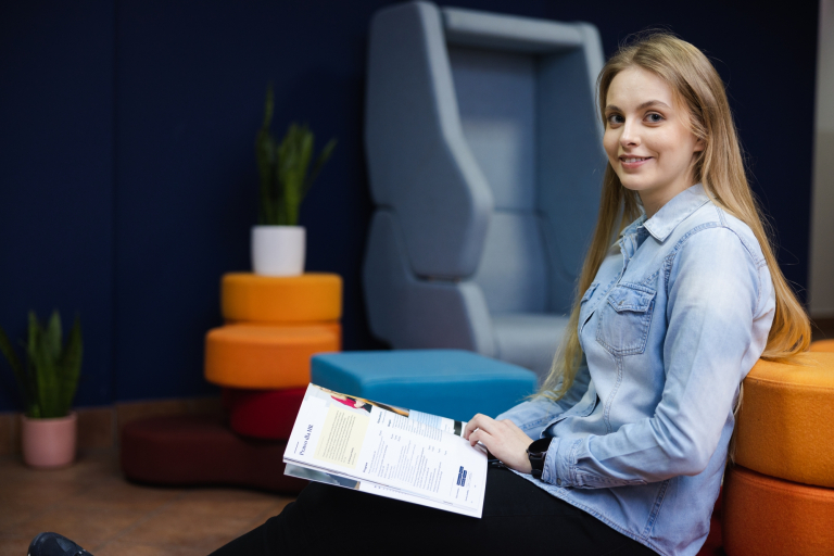 Centrum Języków Obcych | Uniwersytet WSB Merito Łódź: Grafika główna: WSB Merito Łódź, dla nowych studentów, studentka siedzi na sofie i przegląda informator uniwersytetu