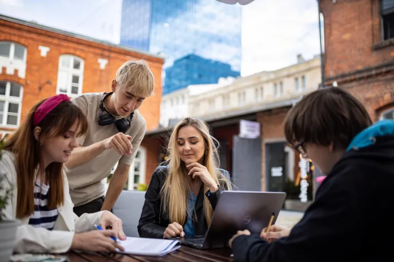 Transport, spedycja i magazynowanie | Studia I stopnia w Łodzi | Uniwersytet WSB Merito Łódź: Grupa młodych osób pracuje wspólnie nad projektem na świeżym powietrzu, korzystając z laptopa i notatek w miejskim otoczeniu.