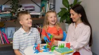 Wyniki wyszukiwania | Uniwersytet WSB Merito Opole: Główna grafika: Opole - specjalność: Praca z osobami niedostosowanymi społecznie z profilaktyką uzależnień - siedząca przy stole kobieta z dwójką dzieci, podczas zabawy rysunkowej 