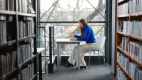 Zamówienia publiczne | Uniwersytet WSB Merito Opole: Główna grafika: Opole - studia podyplomowe - Zamówienia publiczne - Kobieta siedząca w bibliotece