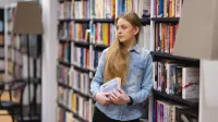Pedagogika resocjalizacyjna z socjoterapią i kryminologią | Studia II stopnia w Opolu | Uniwersytet WSB Merito Opole: Główna grafika: Opole - studia II stopnia - specjalność Pedagogika resocjalizacyjna z socjoterapią - Dziewczyna opierająca się o regał z książkami