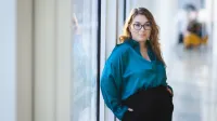 Mediacje sądowe i pozasądowe     | Studia podyplomowe w Opolu | Uniwersytet WSB Merito Opole: główna grafika: Opole - studia podyplomowe - mediacje sądowe i pozasadowe - kobieta w zielonej koszuli stoi przy oknie i patrzy wprost w obiektyw