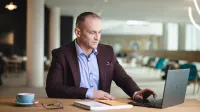 Kompetencje przyszłości - przewaga w świecie zmian | Studia podyplomowe w Opolu | Uniwersytet WSB Merito Opole: Główna grafika: Opole- studia podyplomowe- Kompetencje Przyszłości - Przewaga w Świecie Zmian- uczestnik studiów podyplomowych siedzi przy biurku i spogląda w laptopa