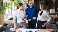 Analiza i informatyka śledcza | Studia podyplomowe w Opolu | Uniwersytet WSB Merito Opole: Główna grafika: Opole - studia podyplomowe - Analiza i informatyka śledcza- uczestnicy studiów podyplomowych stoją przy biurku i rozmawiają