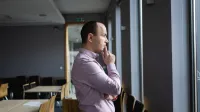 Wykorzystanie zarządzania kryzysowego, obrony cywilnej i cyberbezpieczeństwa w planowaniu i zapobieganiu atakom terrorystycznym | Studia podyplomowe w Opolu | Uniwersytet WSB Merito Opole: Główna grafika-Opole- studia podyplomowe- Wykorzystanie zarządzania kryzysowego, obrony cywilnej i cyberbezpieczeństwa w planowaniu i zapobieganiu atakom terrorystycznym - uczestnik studiów podyplomowych stoi, opierając się o biurko i rozmyśla spoglądając za okno 