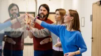 Psychoonkologia | Studia podyplomowe w Opolu | Uniwersytet WSB Merito Opole: Główna grafika: Opole - studia podyplomowe - Psychoonkologia - uczestnicy studiów podyplomowych analizują rozpisane treści na szybie